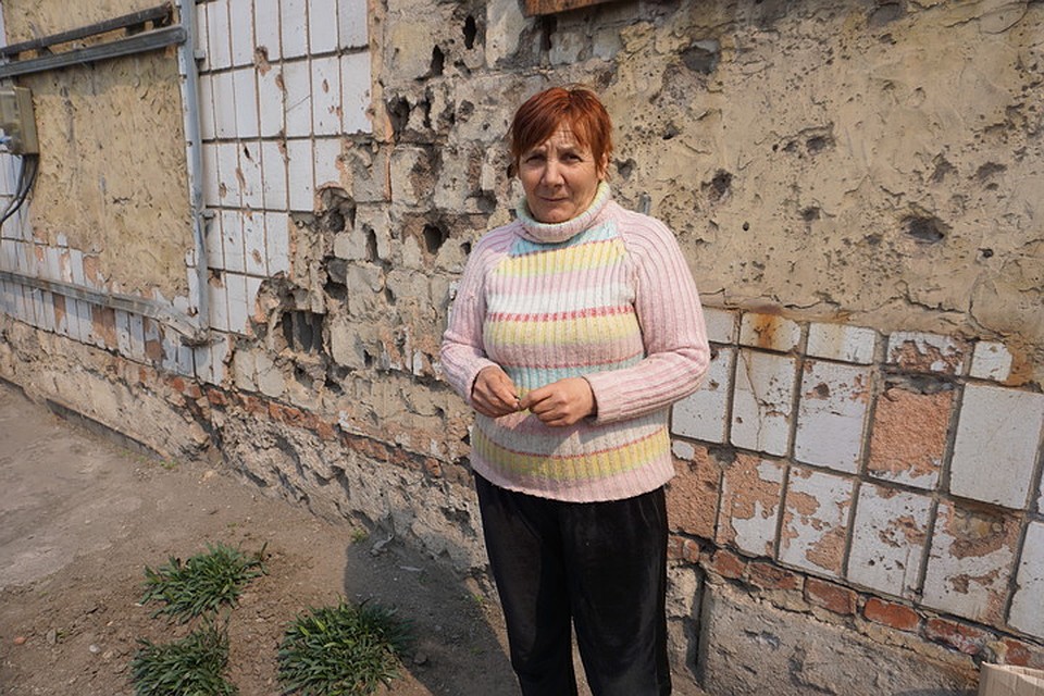 Елена возле стены сельского магазина. Здесь все в следах от осколков. Фото: Юлия АНДРИЕНКО
