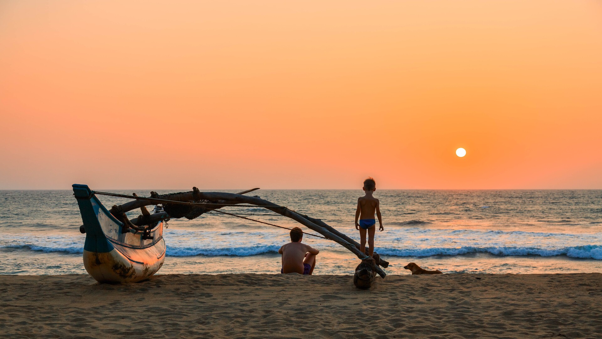 Отец, сын и собака сидят на пляже на закате, Калутара.